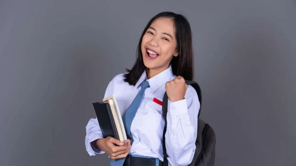 4 - Gambar seorang siswi yang membawa ransel dan buku, tersenyum pada kamera