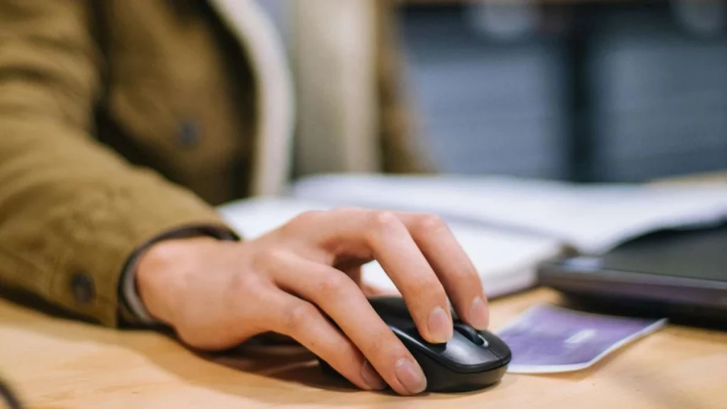 6 - gambar seseorang menggenggam mouse pada meja kerja