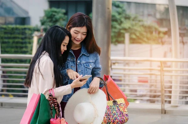 Dua orang perempuan sedang membaca chat sambil menenteng beberapa tas belanja