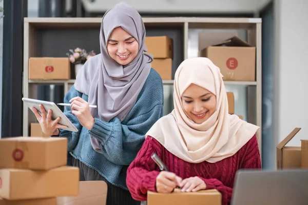 Dua perempuan muslim sedang menulis alamat pelanggan di paket yang akan dikirimkan