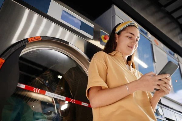 Seorang perempuan sedang membalas chat di tempat laundry