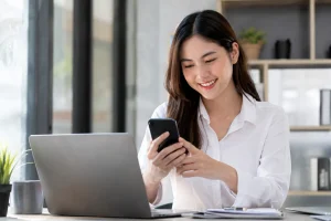 perempuan profesional melihat ponsel di meja kerja dengan laptop terbuka