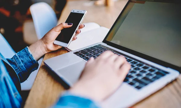 Seseorang sedang memegang ponsel di depan laptop